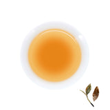 A cup of brewed Bulang Ancient Tree Raw Pu-erh, next to brewed tea leaves