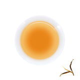 A cup of brewed Yiwu Wild Tree Raw Pu-erh, next to brewed tea leaves