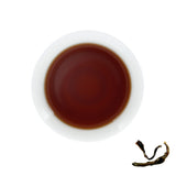 A cup of brewed Menghai Old Tree Ripe Pu-erh, next to brewed tea leaves
