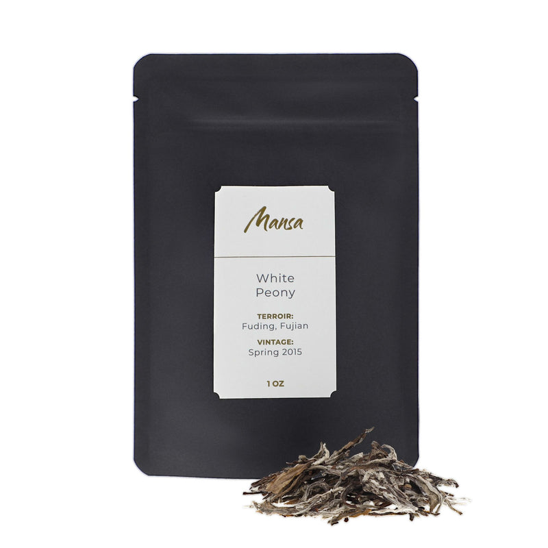 White Peony front packaging photo. A black pouch with a label with a piece of broken tea cake